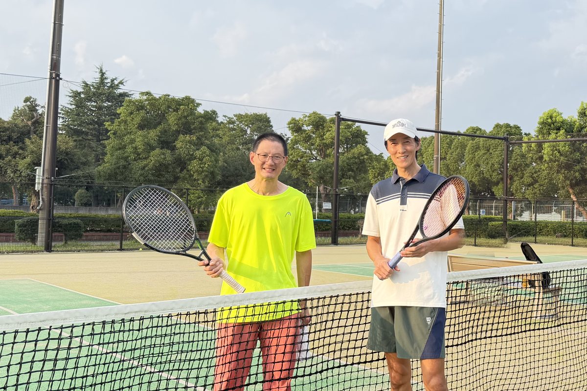 The two hosts of Green Set Tokyo standing at the net on an outdoor court, rackets in hand.